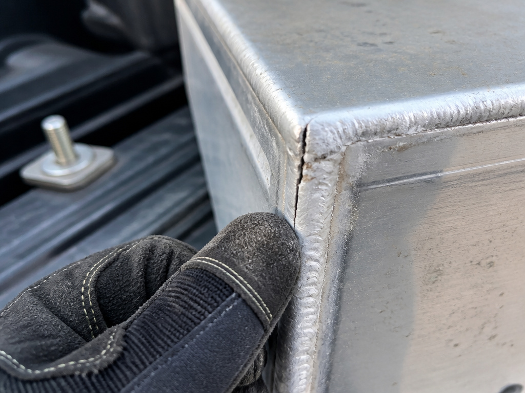 Close-up inspection of a cracked weld on a truck bed toolbox corner.