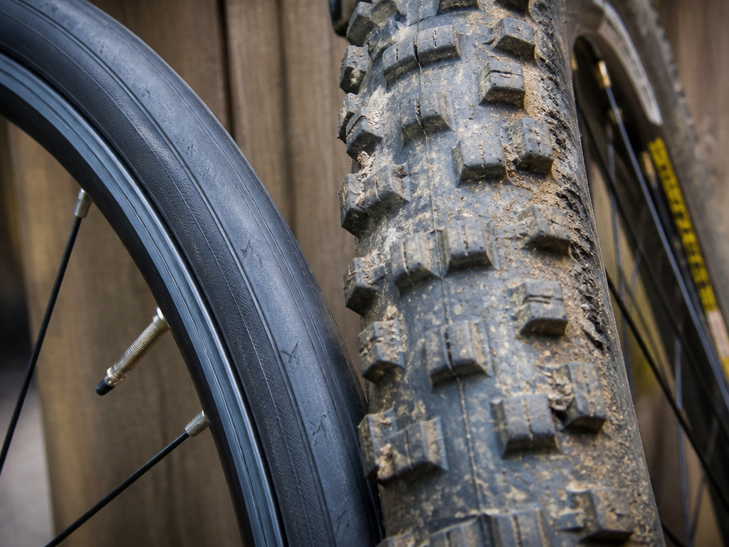 Close-up comparison of narrow road bike tire versus wide knobby mountain bike tire.