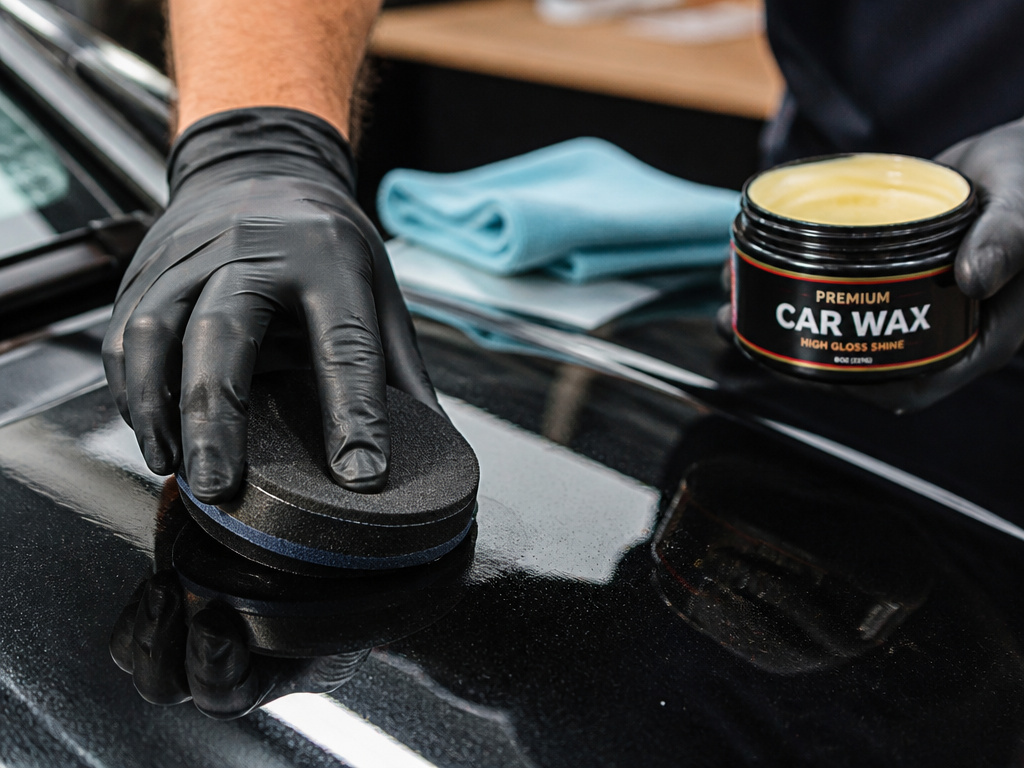 Person applying protective wax to the hood of a used black car.